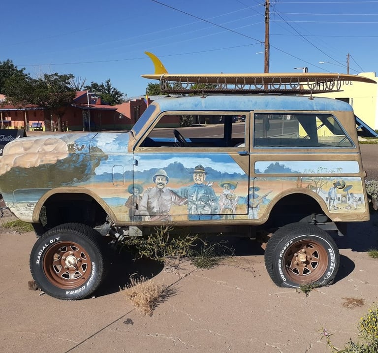 Broken-down sand buggy parked with a surfboard strapped on top.