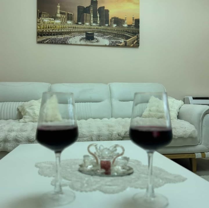 Two glasses of red wine on a coffee table in a living room with a Kaaba wall art print.