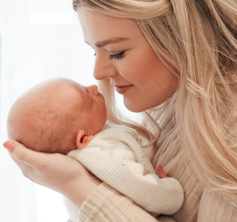Newborn baby sleeping in mother’s arms, neutral tones, natural light