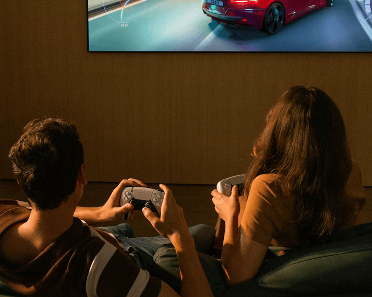 two people sitting on a couch holding video game controllers facing the tv