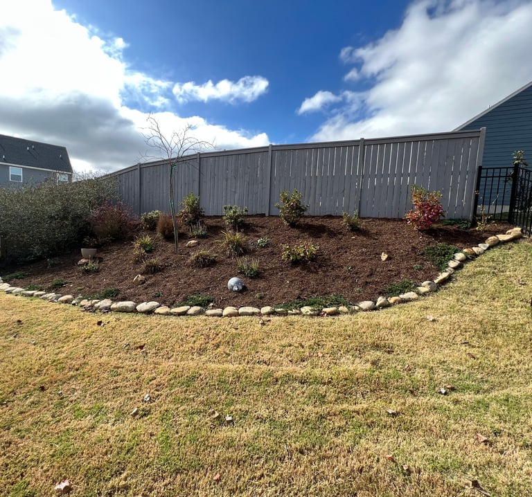 Flower bed on a side hill with various shrubs, brown mulch and large cane rock for a stone border