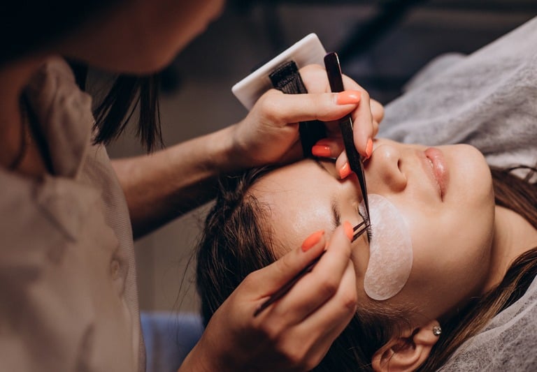 Professional lash artist applying individual eyelash extensions using precision tweezers in a beauty salon.