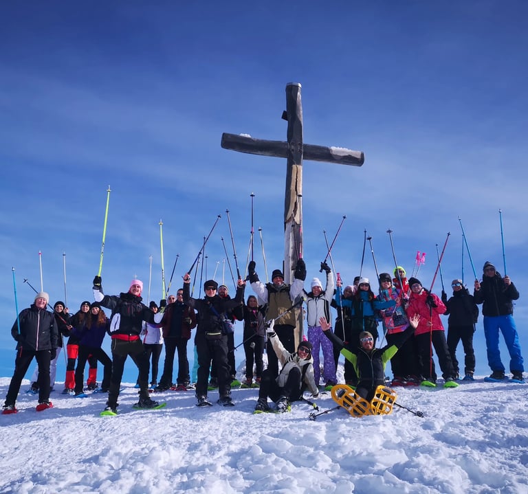 Gruppo di ciaspolatori sotto la croce del rifugio Cima Alta alle Pendici del Gran Sasso con le bacchette da sci verso l'alto 