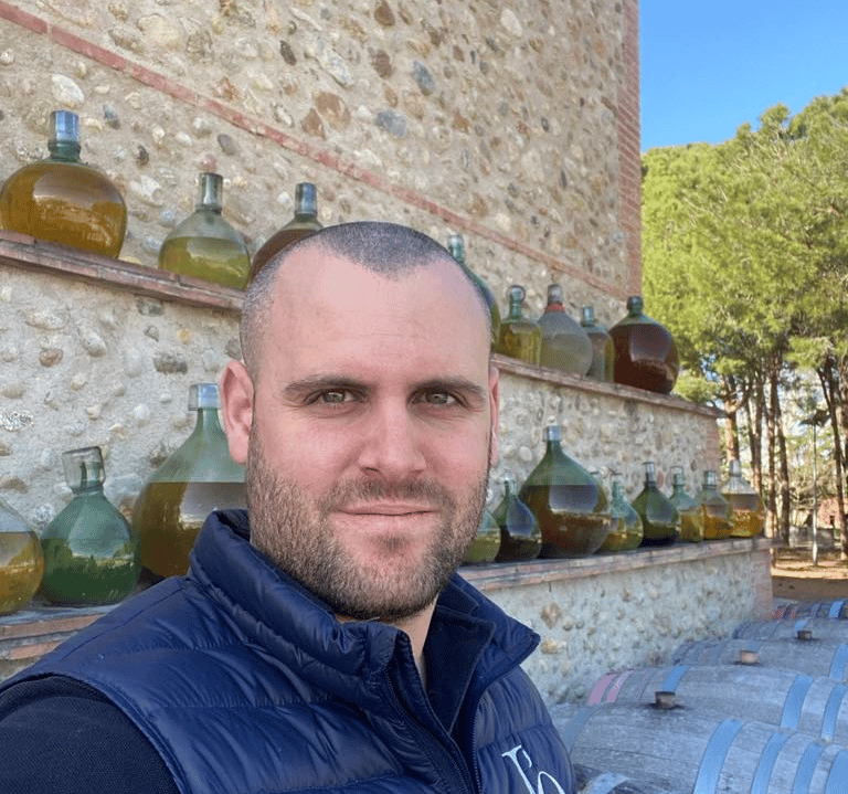 a man in a vest and vest standing in front of a wine barrel