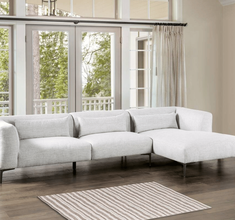 Modern light gray sectional sofa with chaise lounge on dark wood floors in a bright living room.