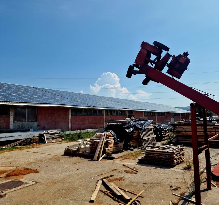 production site with solar panels on the roof and a pile of wood in the yard
