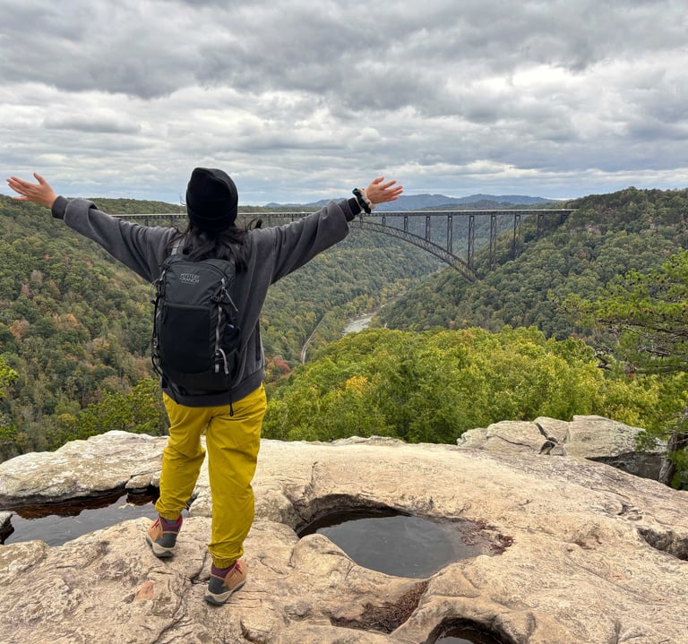 Person with outstretched arms enjoying the view at New River Gorge, West Virginia, surrounded by mou