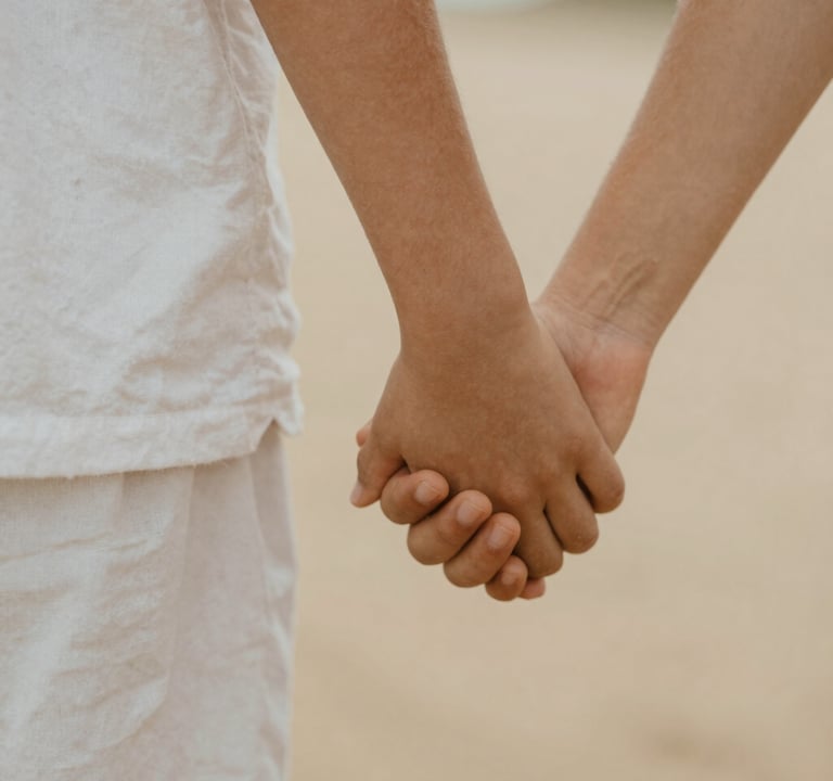 A close-up, rectangular photograph of a child's hand holding a parent's hand. The scene is shot in a warm, sun-drenched environment with a cinematic, soft-focus background. The tones are natural, featuring white linen textures and soft sand-colored skin tones. Authentic and emotional.