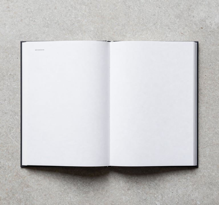 A minimalist flat-lay of an open photography book with white pages on a light gray stone surface. The composition is perfectly symmetrical, capturing the clean, editorial aesthetic of a modern North American art publication house.
