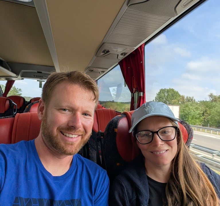 Moose and Bugs taking a selfie while traveling on a modern tour bus with red seats.