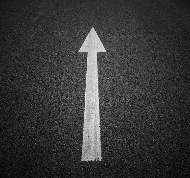 a white arrow pointing up to the left side of a road