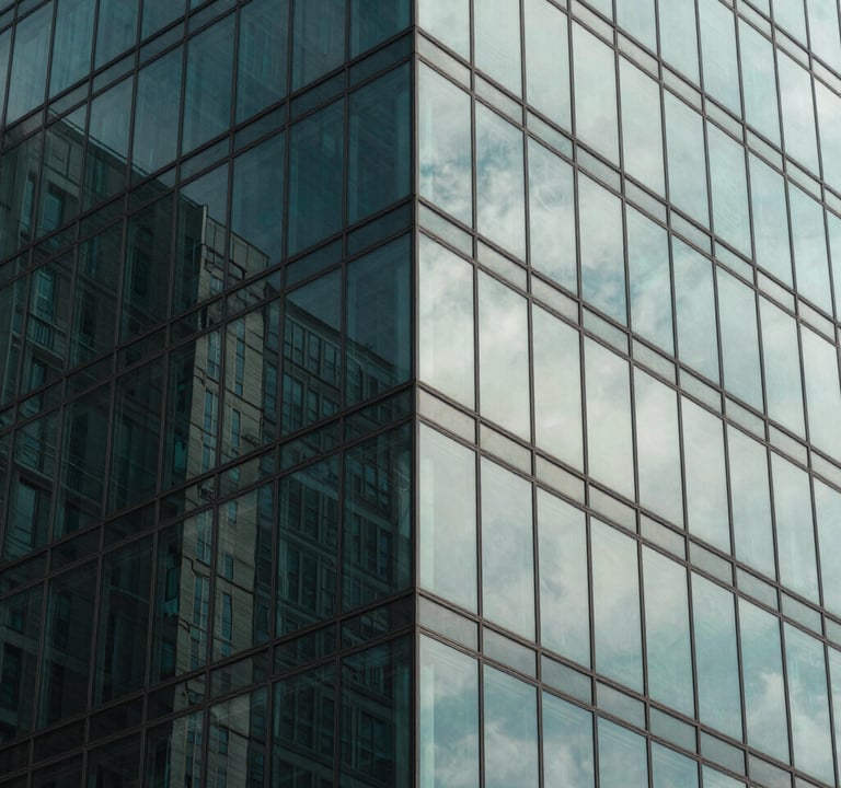 Abstract architectural photography of a glass skyscraper corner. Reflections of the sky in deep muted teal and soft sage are visible on the surface. The lines are sharp and perfectly aligned, emphasizing a clean, modern aesthetic.