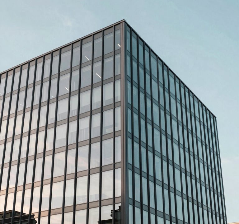 An architectural photograph of a minimalist International / Western glass building reflecting a soft sky blue sky. The image emphasizes clean lines and modern structural precision.