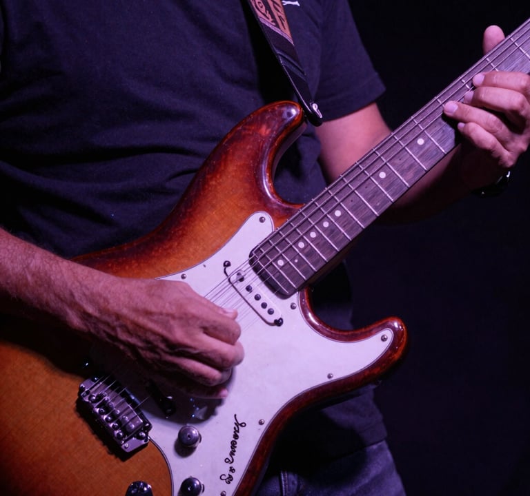 A close-up artistic photography shot of hands playing a vintage electric guitar, South American / Venezuelan context, deep shadows with dusty purple and rose lighting, reflecting a rock and soul vibe.