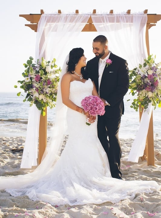 bride and groom standing under floral decorated arbor on the beach