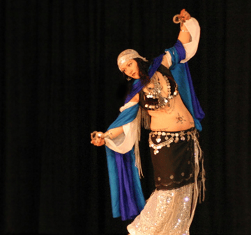 Shahravar Arabic style dancer wearing coin bedlah playing finger cymbals while wearing a white spark
