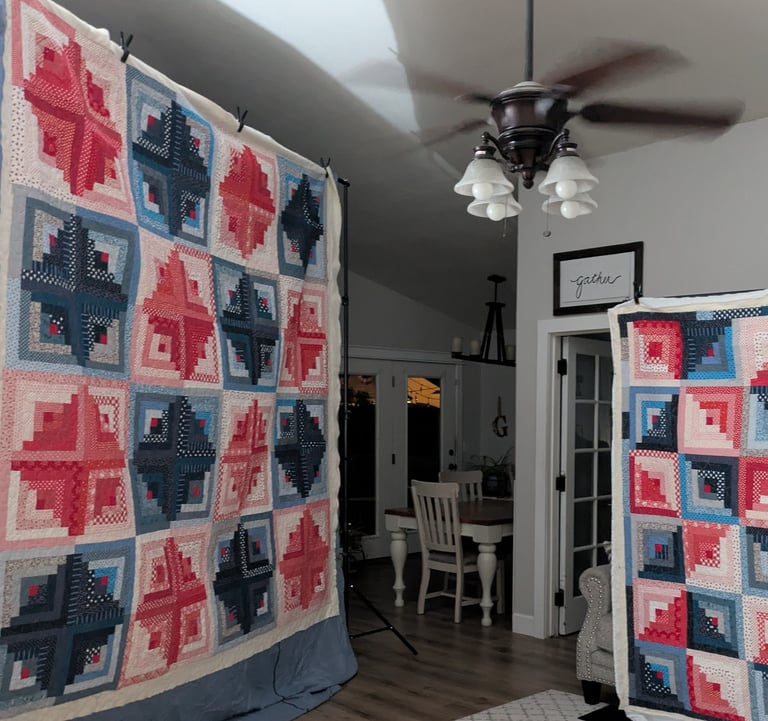 Two red white and blue colorful log cabin quilts on display stands in a cozy room with wood floors.