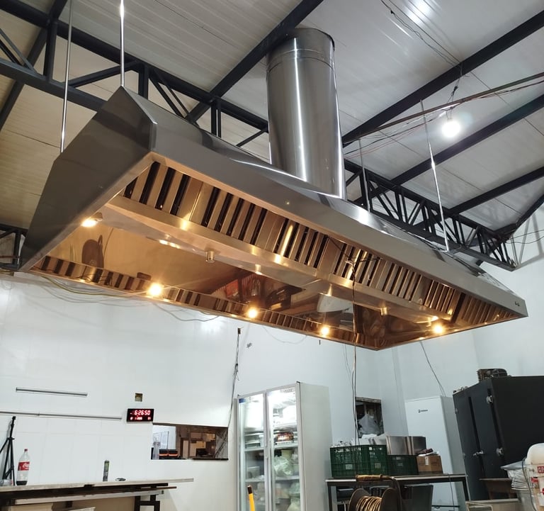 Stainless steel commercial kitchen exhaust hood with lights installed over a food preparation area.