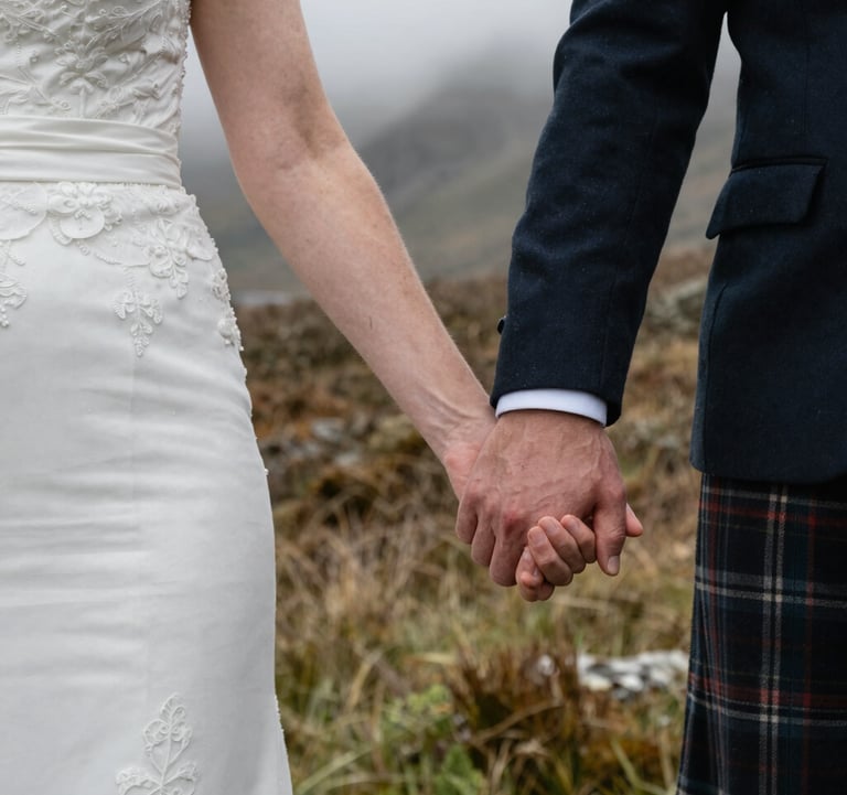 A close-up photograph of a Northern European / Scottish bride and groom holding hands during an elopement ceremony in a wild, misty glen.