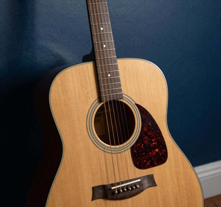 A detailed close-up of a weathered acoustic guitar leaning against a dark blue studio wall, featuring soft shadows and golden hour lighting, North American coastal aesthetic.