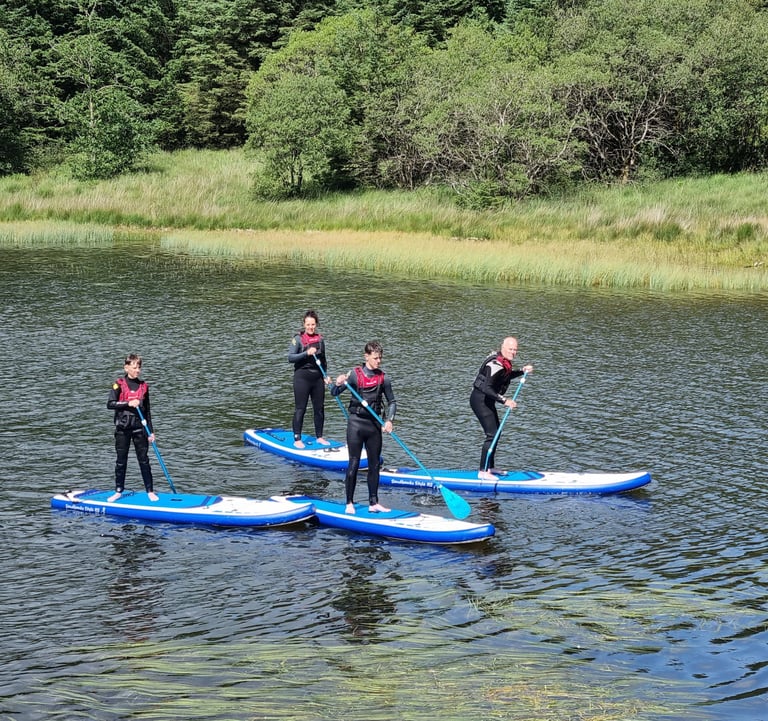 A group of stand up paddle boarders on a lake with lush green vegetable surrounding it