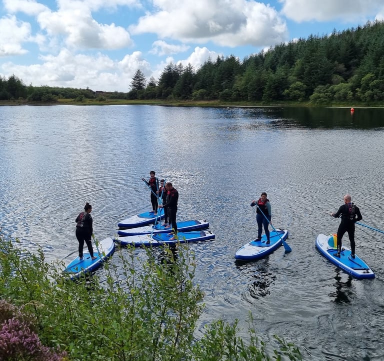 A group of paddle boarders on a calm lake surround by pine forest.