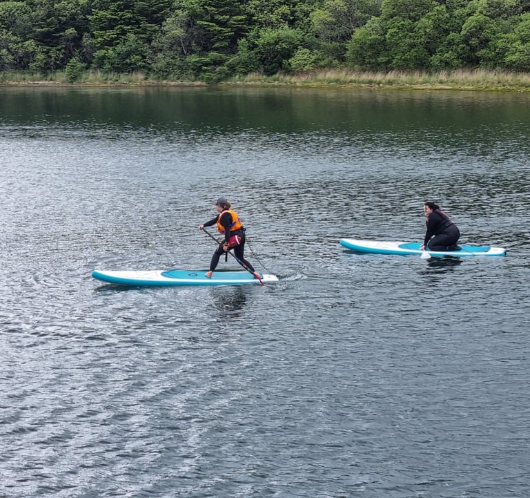 A stand up paddle board instructor demonstrating a step back turn while a student watches