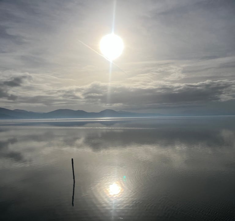 lago trasimeno with a bright sun shining through the clouds