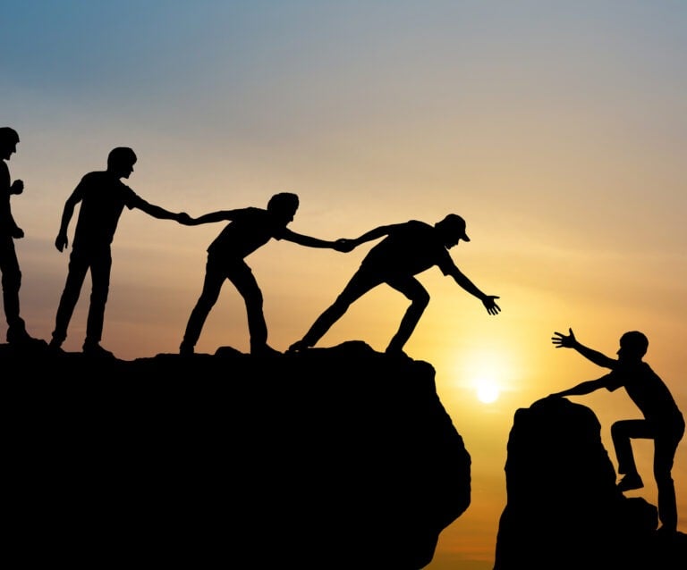 Silhouettes helping other climb a mountain, symbolizing community and addiction recovery support