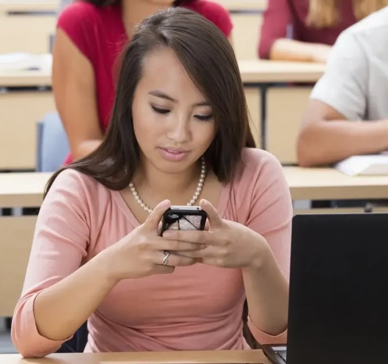 a woman sitting at a desk with a laptop and a cell phone