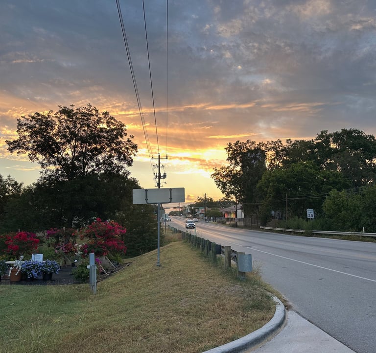 Flower booth and display beside sunset over highway in small town.