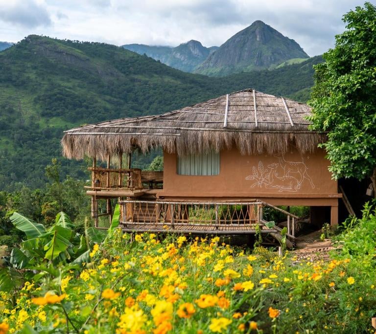 Mud house stay in Kerala with mountains in background.