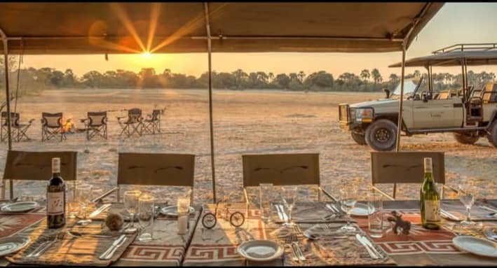 Luxury safari dinner table set outdoors in the African Karoo during a sunset game drive.