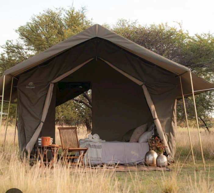Luxury safari glamping tent with comfortable bedding and wooden furniture in the African Karoo.