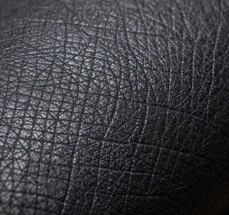A macro photograph focusing on the rich texture of high-quality dark charcoal leather with subtle metallic gold thread details, symbolizing premium craftsmanship and luxury trade.