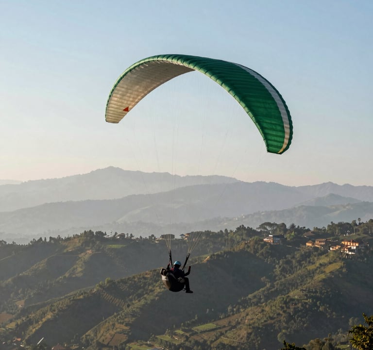 A wide-angle shot of a paraglider in flight over the lush hills of Godawari, Lalitpur. In the background, the distant Himalayan range is visible under a clear sky. The paraglider wing has accents of muted forest green.