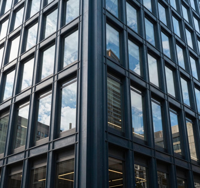 Professional photography of a modern commercial office building exterior in a US downtown area, with clean architectural lines and bright daylight reflecting off charcoal blue steel elements.