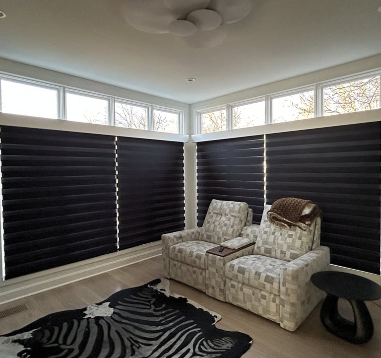 Modern living room featuring black roman shades, patterned reclining chairs, and a zebra print area rug.