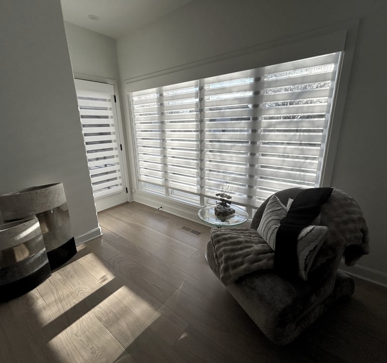 Modern living room featuring zebra blinds on large windows, hardwood floors, and a plush armchair.