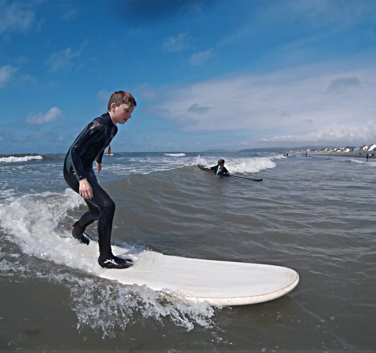 A young male surfing standing up riding a wave with sunshine and blue skies