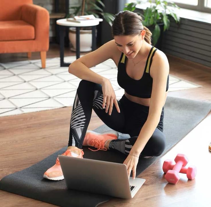 Mulher sorridente com roupa de ginástica fazendo exercícios em casa com tapete de yoga e halteres 