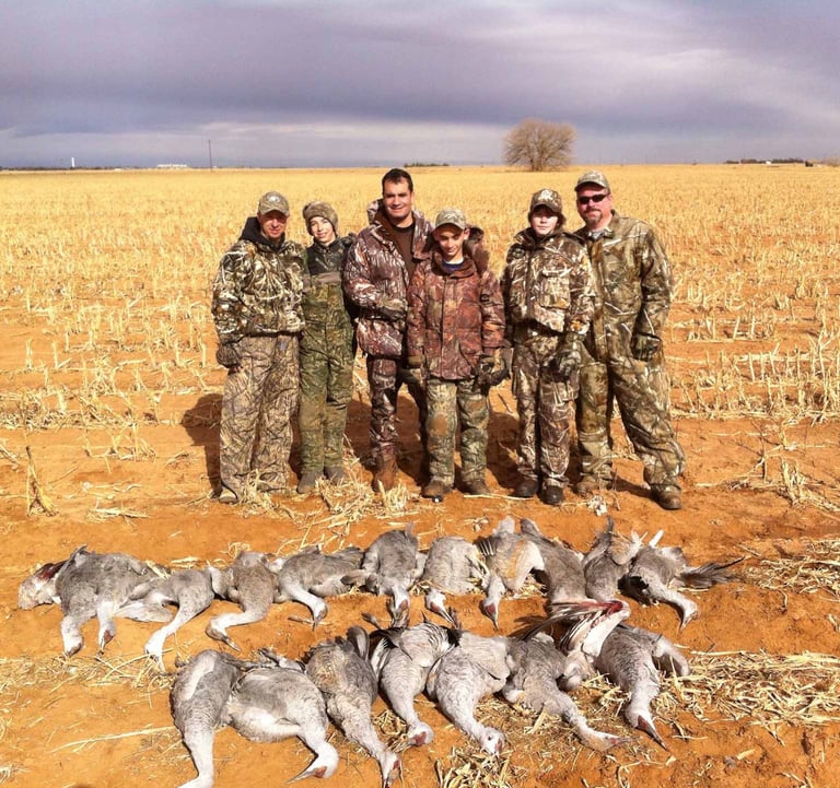 Four hunters in camouflage posing with their limit of Sandhill Cranes after a successful Texas Panhandle hunt.