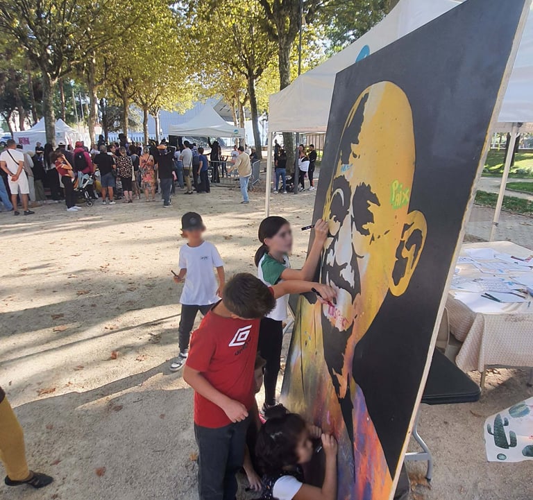 Children painting a large street art portrait of Mahatma Gandhi at an outdoor community festival.