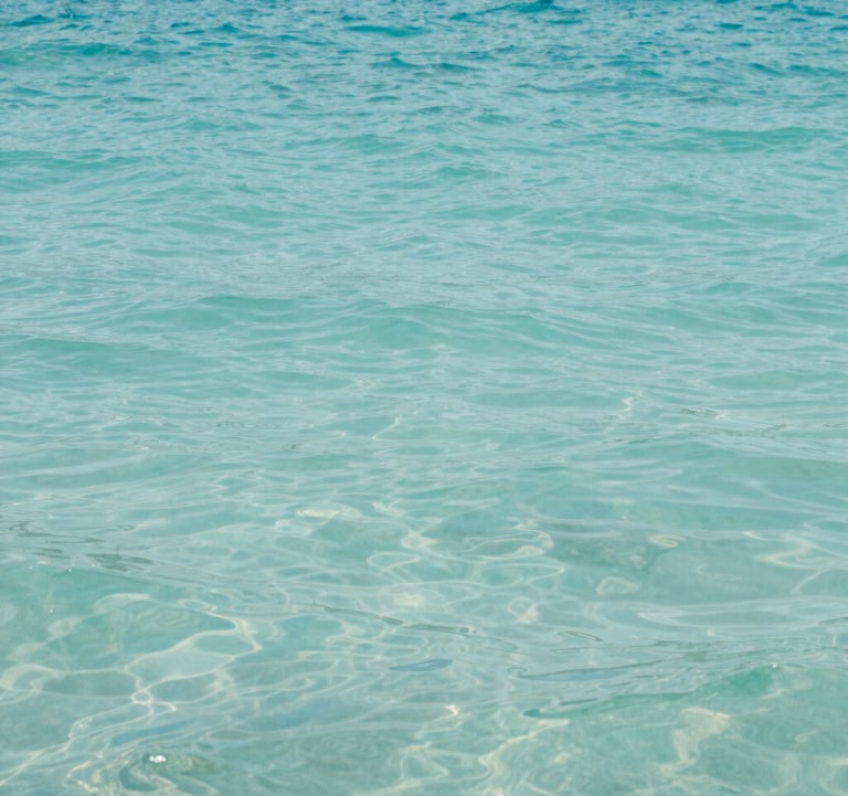 A tranquil, curated view of a coastal retreat with turquoise water. The composition is elegant and calm, featuring the soft blue-green hues of #A8C9CF. The lighting is bright and natural, reflecting an authentic travel experience.