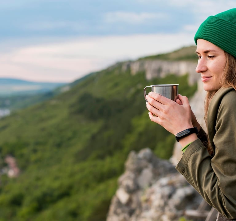 Uma mulher jovem segurando uma xícara admirando o horizonte no alto de uma montanha