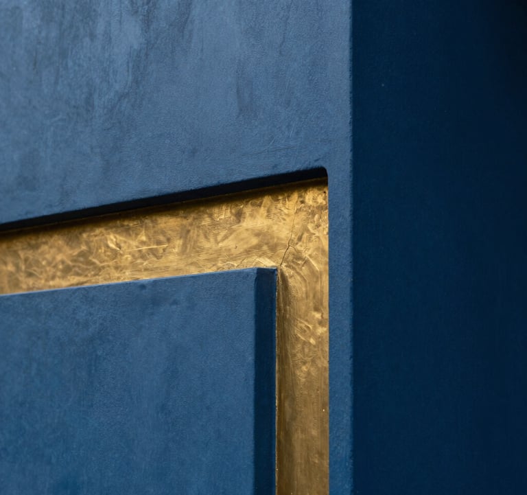 Architectural detail of a luxury Indian estate in Lonavala. A smooth, deep blue concrete wall meets a warm gold metallic inlay. The lighting is soft and indirect, creating a sense of depth and premium texture. 8k close-up photography.