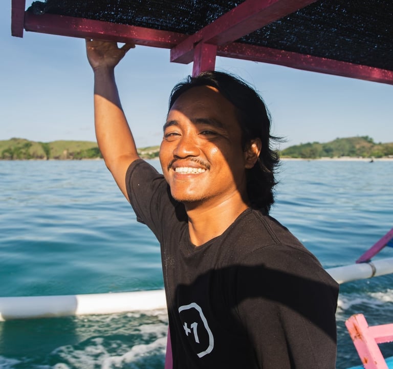 Our surf instructor smiling on a traditional boat on the blue ocean water in Lombok, Indonesia.