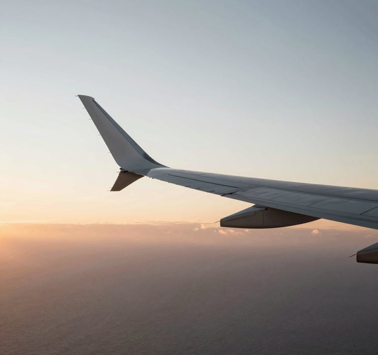 An artistic, high-contrast shot of an airplane wing slicing through a sunset sky over the Atlantic. Golden hour light hitting the wing, minimalist and aspirational, #FAF8F5 and #2C3539.