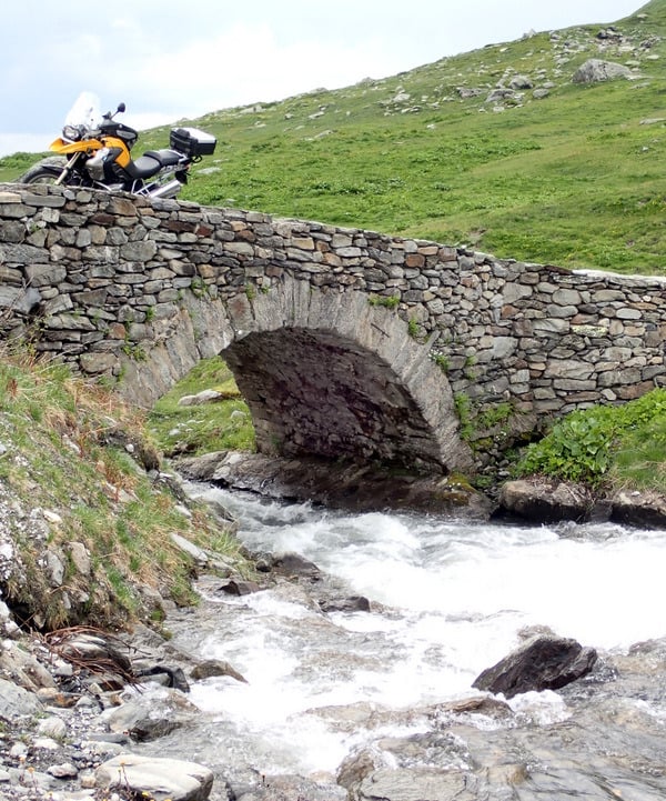 a motorcycle parked on a rocky bridge over a stream