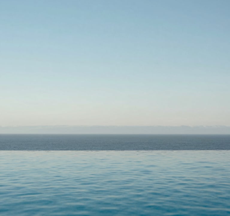 A serene infinity pool reflecting a soft light blue sky, part of a high-end coastal estate in North America, clean and minimalist design.